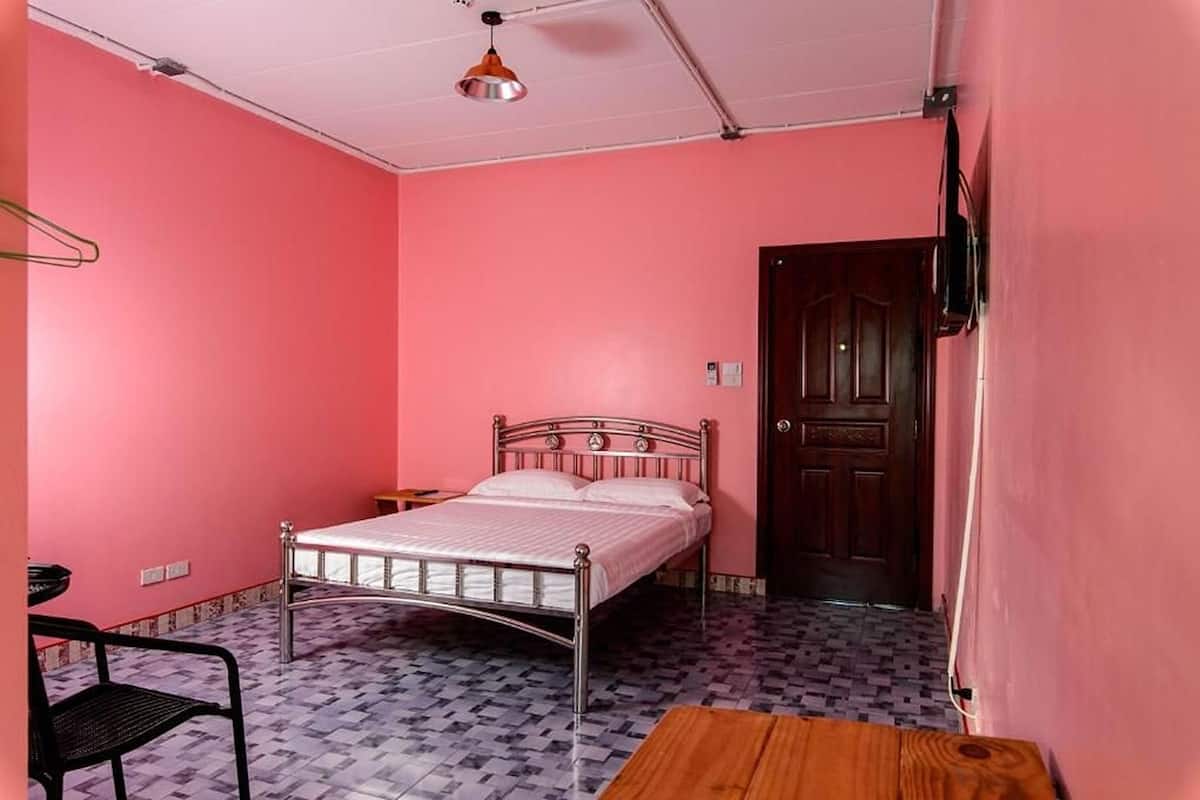 A room with a metal bed, a wooden table, a chair, a hanging lamp, and a door.