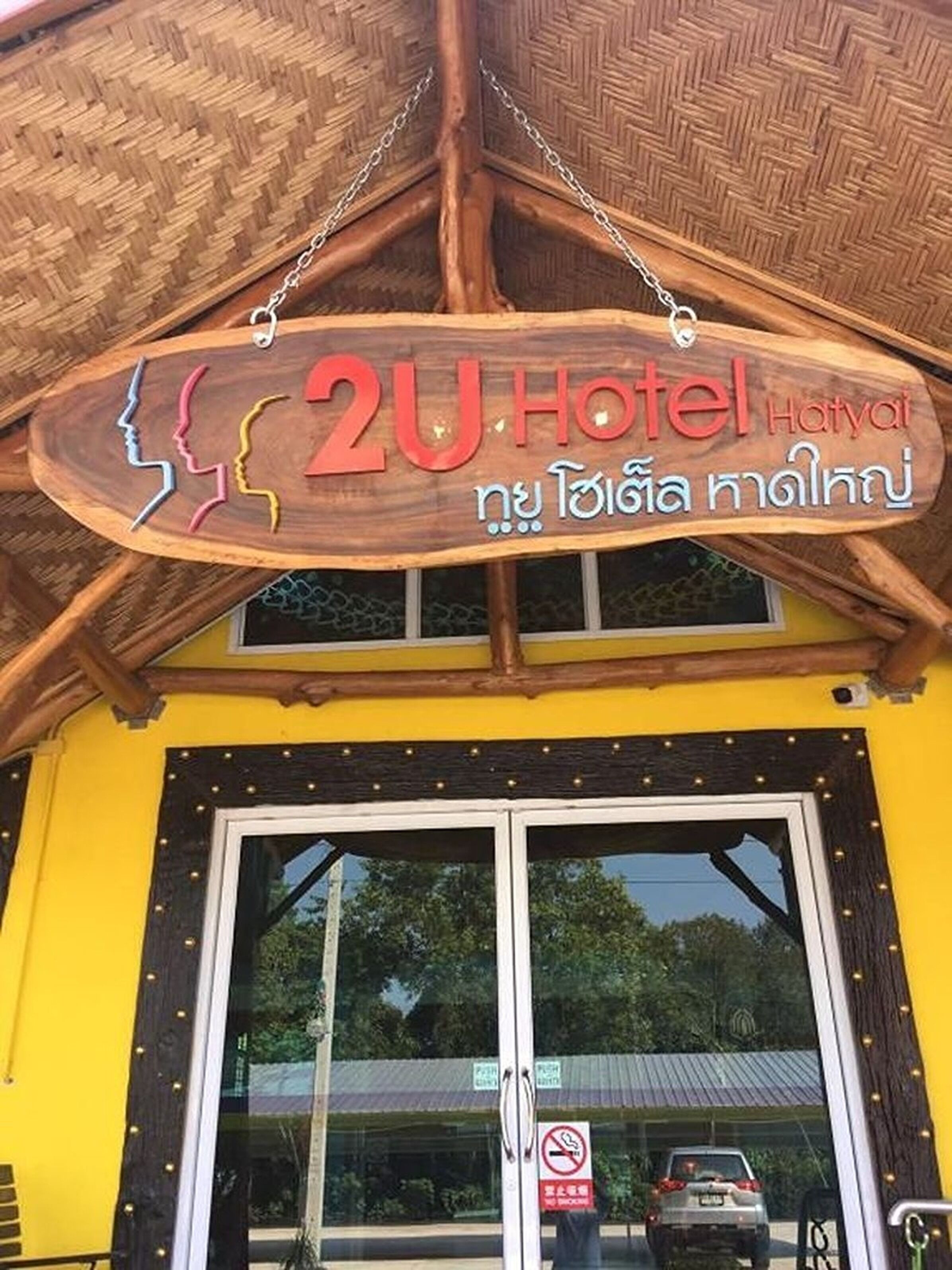 A wooden sign with "2U Hotel Hatyai" and Thai script, indicating a hotel entrance.