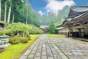 A traditional Japanese temple with a stone pathway leading to a central shrine, surrounded by lush greenery and tall trees. - Kongo Sanmaiin (Koya)