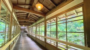 A corridor with wooden beams and large windows offering views of a lush green forest. - Kongo Sanmaiin (Koya)