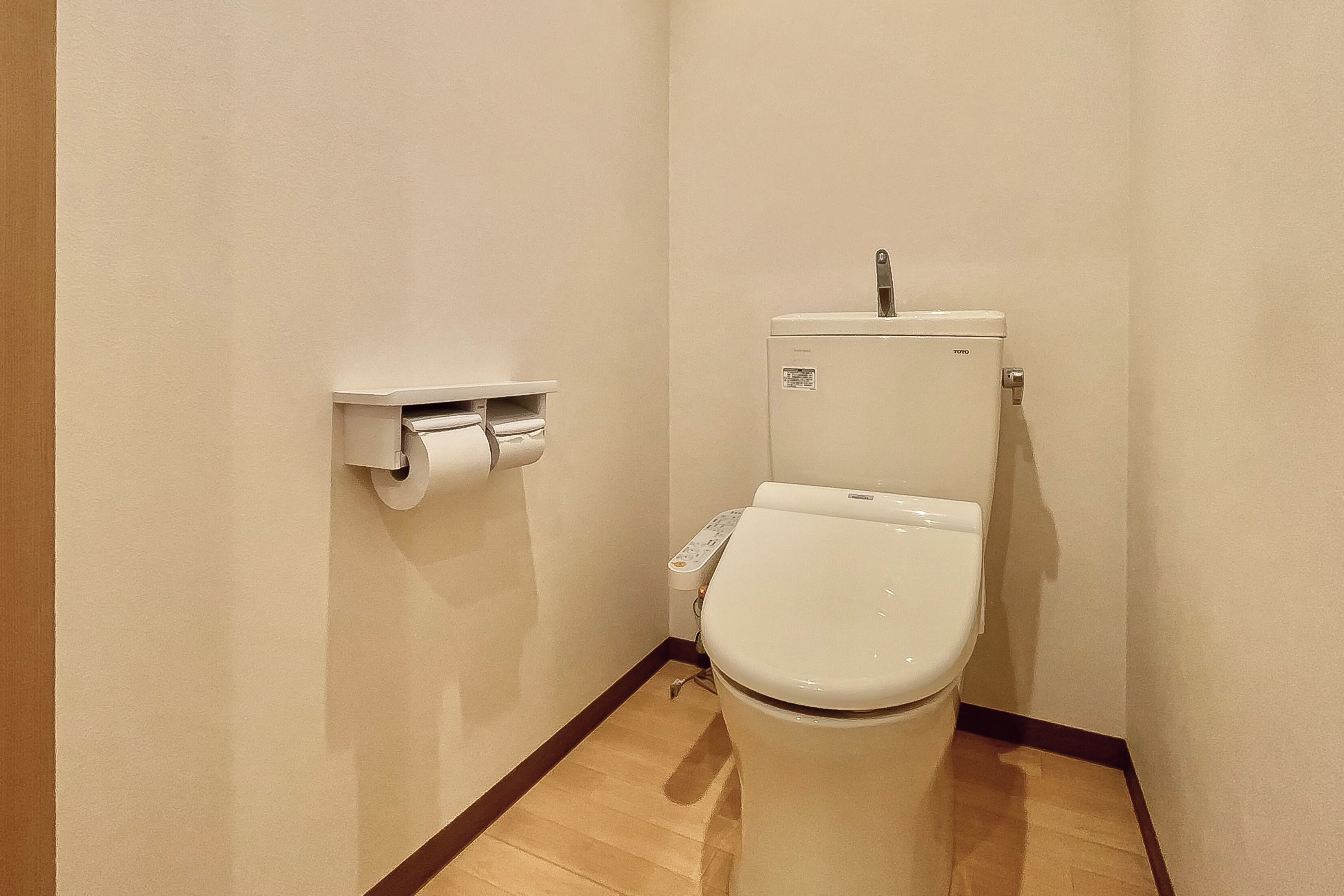A small, clean bathroom with a toilet, a toilet paper holder, and a control panel.