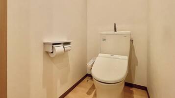 A small, clean bathroom with a toilet, a toilet paper holder, and a control panel.