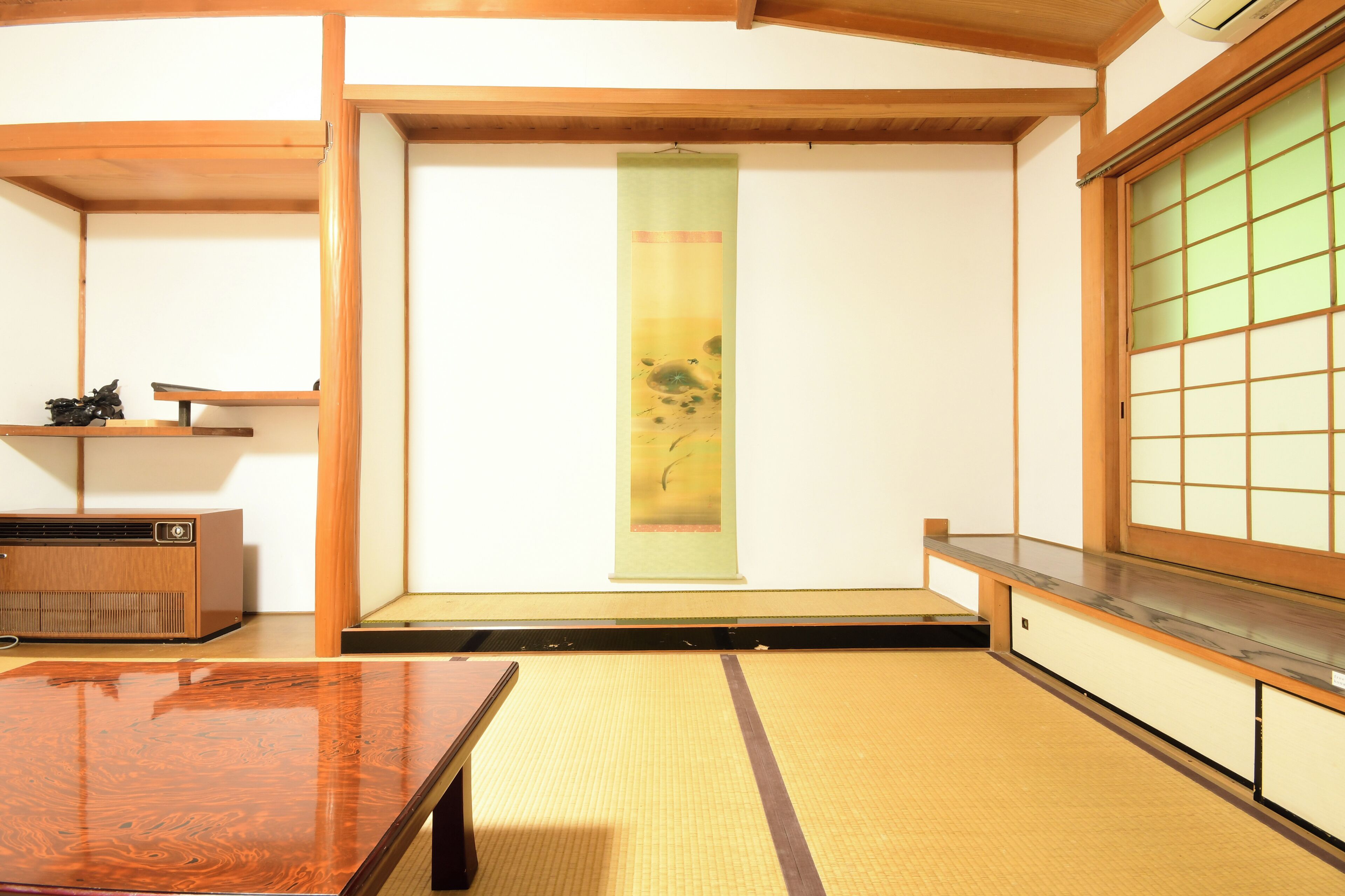 A traditional Japanese room with tatami flooring, a low wooden table, a sliding door with a green screen, and a small shelf with a radio.