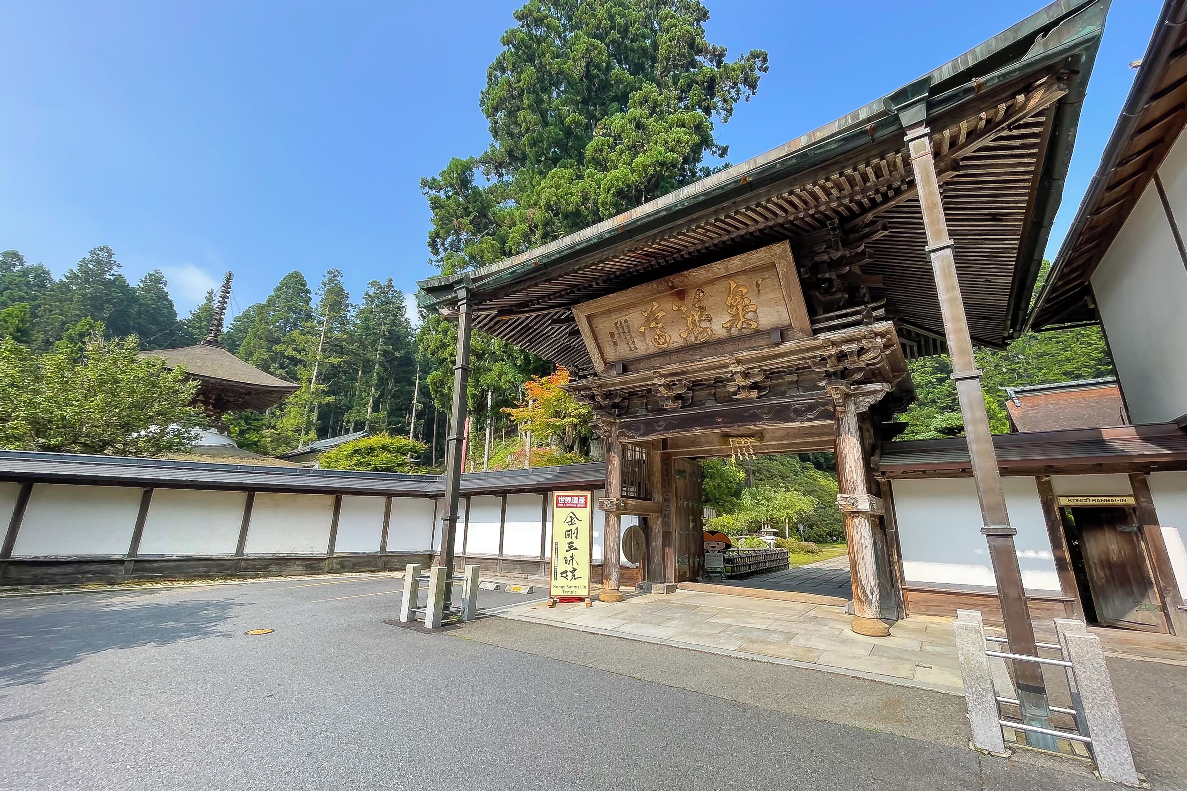Un portón tradicional japonés con pilares de madera y techo de tejas, que da paso a un edificio de fachada blanca.