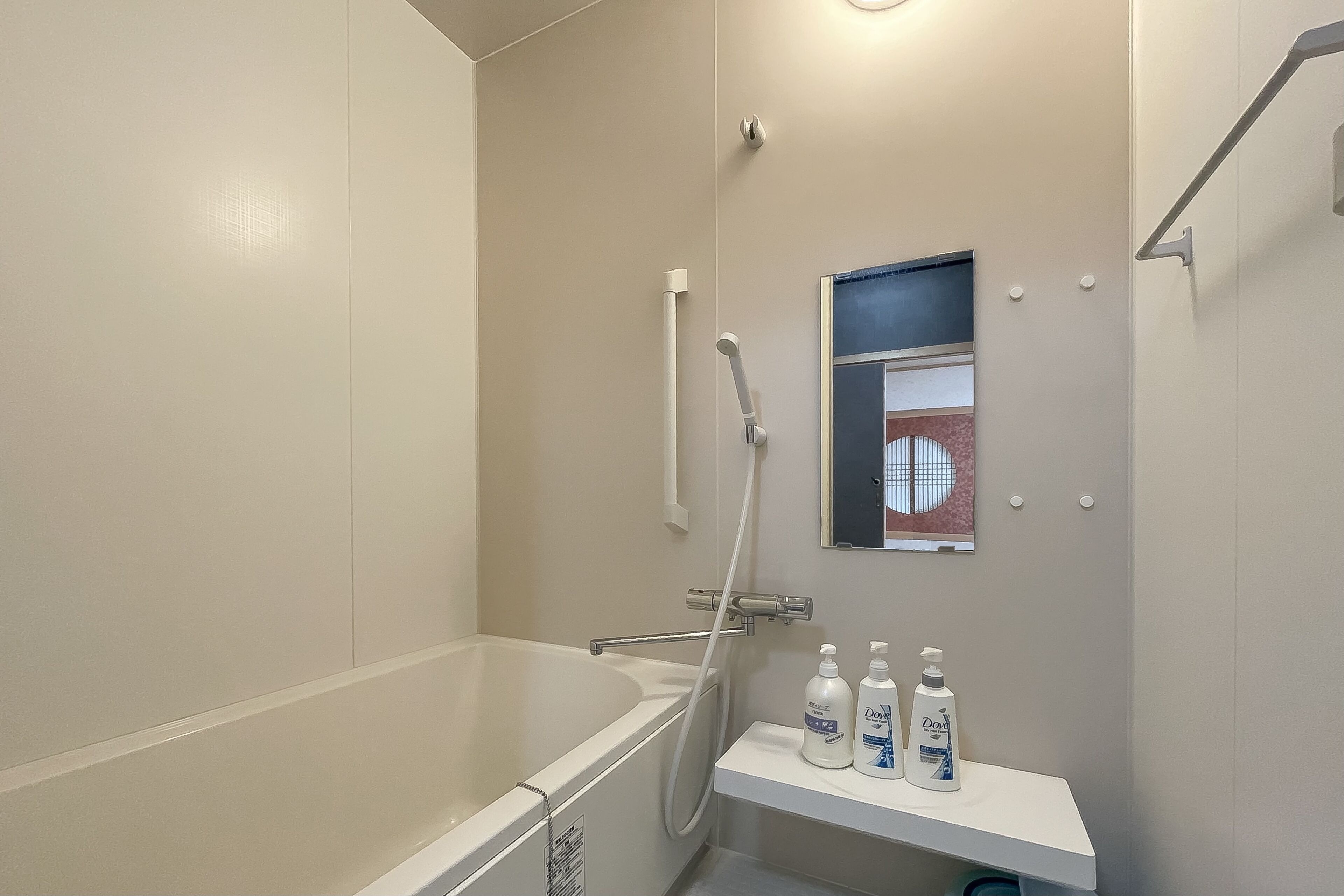 Une salle de bain équipée d’une baignoire, d’une douche et d’une étagère sur laquelle se trouvent deux bouteilles de gel douche Dove.