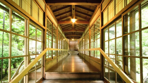 A wooden staircase with glass railings leading to a covered area with a wooden ceiling and a light fixture. - Kongo Sanmaiin (Koya)