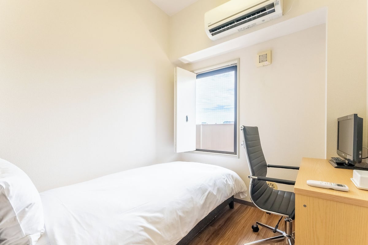 Une chambre d’hôtel équipée d’un lit, d’un bureau avec un ordinateur, d’une chaise et d’un appareil de climatisation.