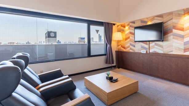 Ein modernes Hotelzimmer mit großem Fenster, einem flachbildfernseher an einer Wand mit Fischgrätmuster, einer Couch und einem Holztisch.