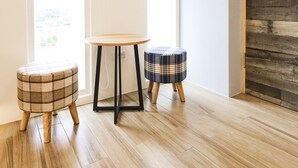 A room with wooden flooring, a plaid ottoman, a small round table, and a wooden door. - Amethyst Bay 2 (Magong)
