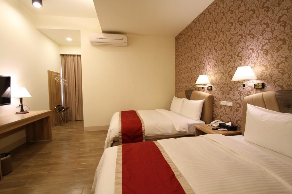 A hotel room with two beds, a desk, a TV, and a bathroom visible through a door.