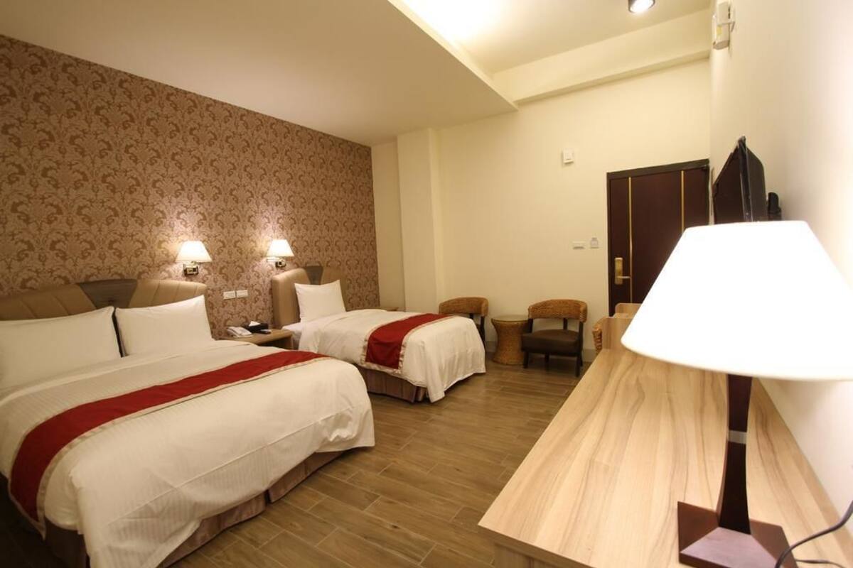 A hotel room with two beds, a desk, a chair, and a TV.