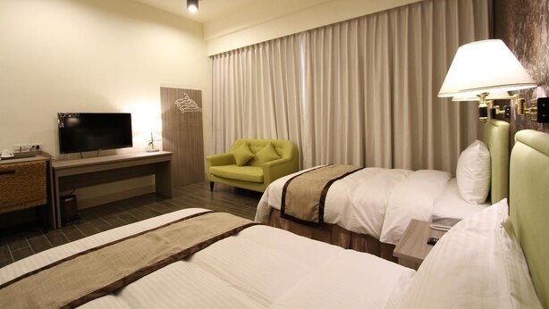 A hotel room with two beds, a desk with a television, a green armchair, and a large window with curtains. - Silia Hostel (Ji'an)
