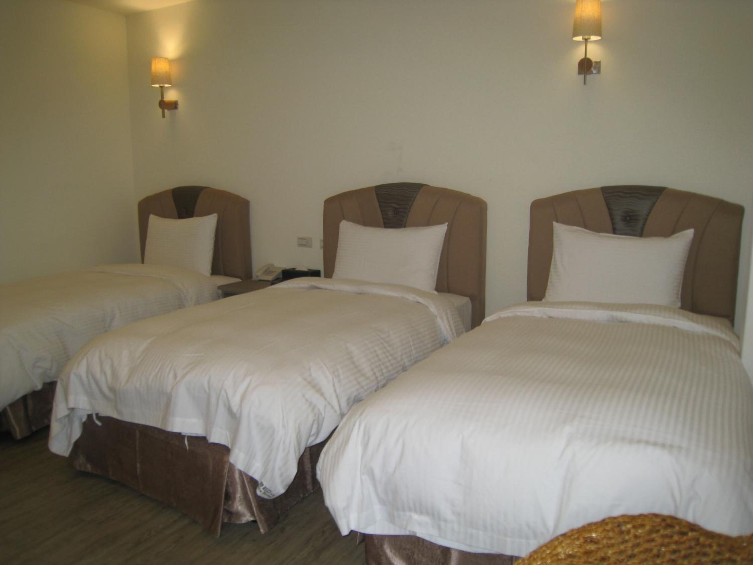 Een hotelkamer met drie eenpersoonsbedden, elk met hoofdeinde en nachtkastje.