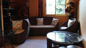 A cozy living area with wicker furniture, a glass table, and a window with curtains. - RM Guest House (Dumaguete)