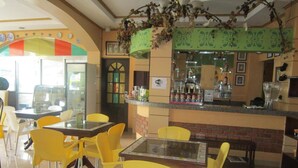 A restaurant with yellow chairs and tables, a bar area with a green decorative hanging, and a Wi-Fi sign. - RM Guest House (Dumaguete)