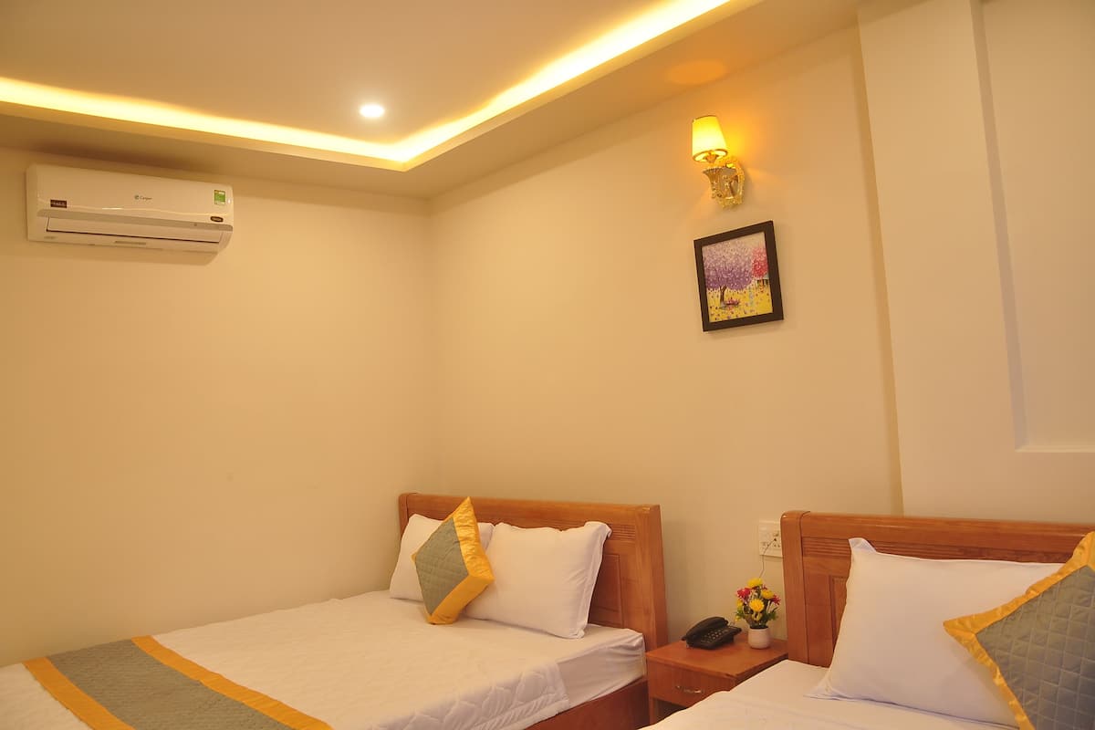 Habitación de hotel con dos camas, aire acondicionado, una mesita de noche con un teléfono y flores, y una lámpara de pared.