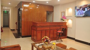 A reception area with a wooden reception desk, a TV screen, and a flower vase on a table.