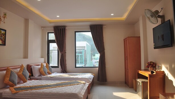 A hotel room with two beds, a desk, a TV, and a window with curtains.