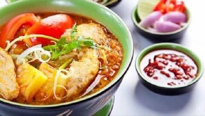 A bowl of soup with various ingredients, accompanied by a small bowl of sauce and a plate of vegetables.