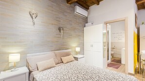 Un dormitorio con una colcha estampada, una mesita de noche con lámpara, un adorno en la pared y un armario.