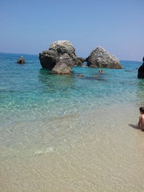 A beach with clear turquoise water, large rock formations, and a person standing on the shore. - B&B in an old farmhouse surrounded by greenery, 400 from the sea and 1 km from Tropea (Parghelia)