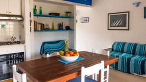 Un espace de vie compact comprenant une table à manger en bois, un canapé et un coin cuisine équipé d’une cuisinière et d’étagères.