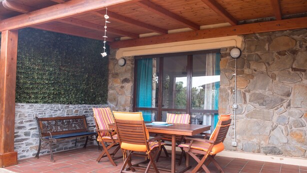 Un patio couvert avec un mur en pierre, un banc en bois et une table avec des chaises.