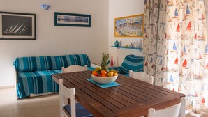 Un coin repas avec une table en bois, un saladier de fruits, un canapé à rayures et une décoration sur le thème de la marine.