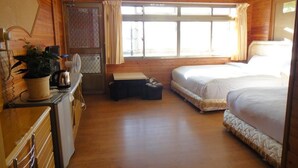 A room with wooden walls and floors, a bed with white bedding, a desk with a kettle, and a window with curtains.