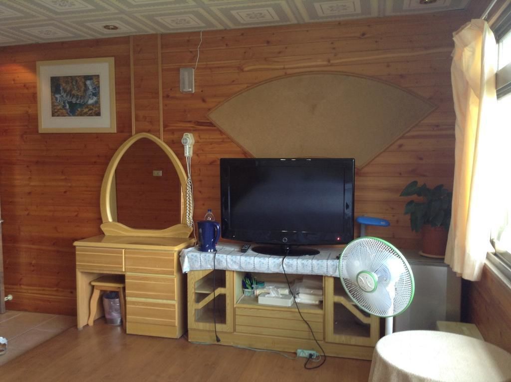 Una habitación de madera con televisión, ventilador y escritorio con cajones.