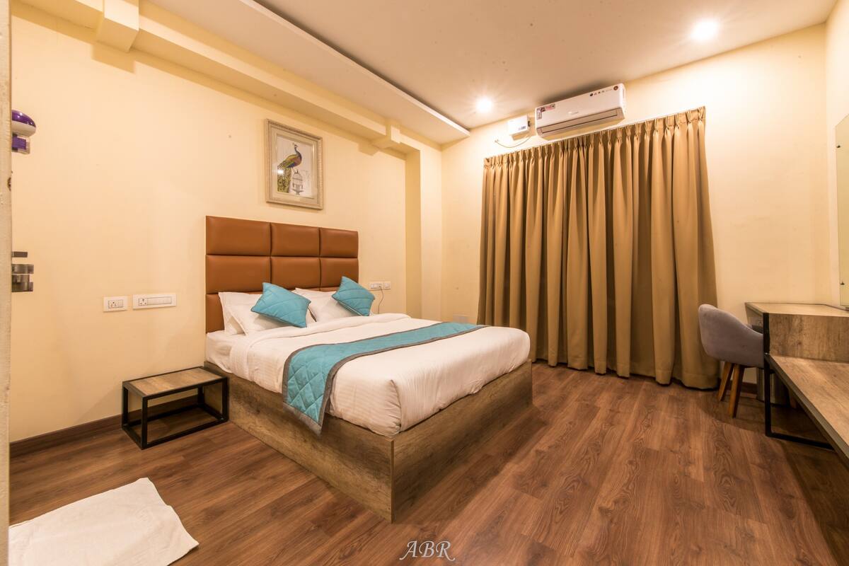 A hotel room with a wooden bed, a desk, and an air conditioning unit.