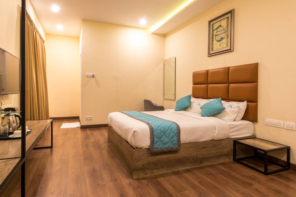 A hotel room with a wooden bed, a bedside table, a TV, and a window with curtains.