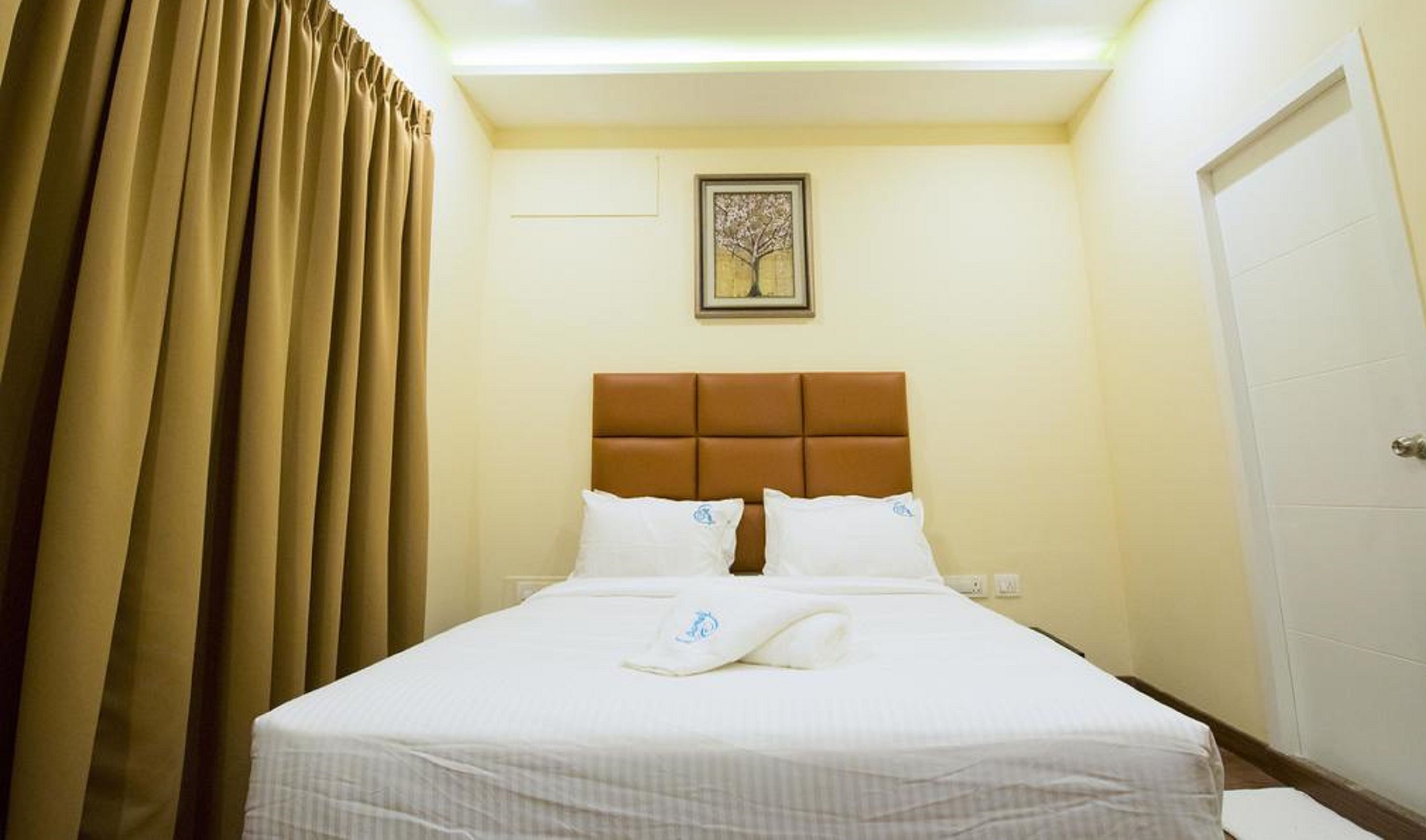 Una habitación de hotel con una cama, un cabecero, un cuadro en la pared y una puerta.