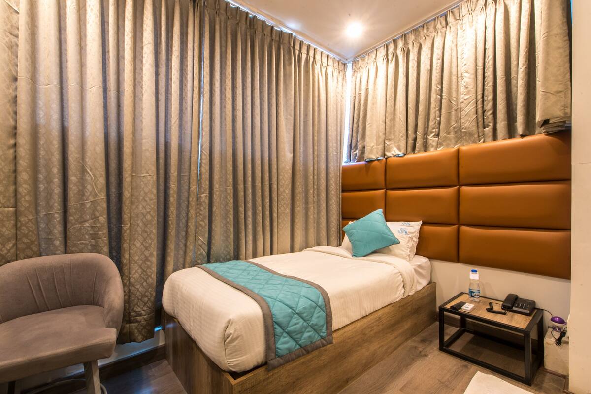 A hotel room with a bed, a chair, a nightstand, and curtains.