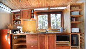 A compact kitchen with wooden cabinets, a built-in microwave, and a window providing natural light. - Free Spirit Pods (North Bruny)