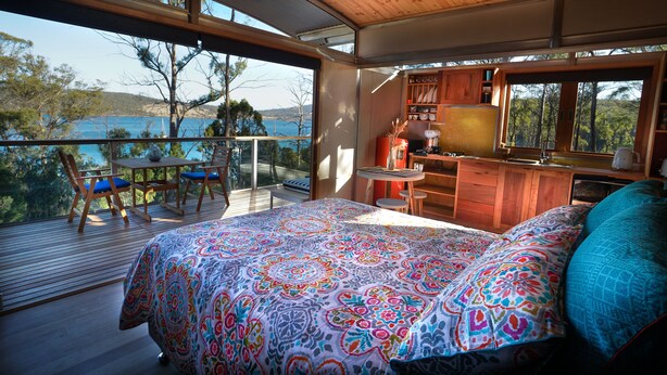 A bedroom with a large bed, a balcony with a view of the sea, and a small kitchen area. - Free Spirit Pods (North Bruny)