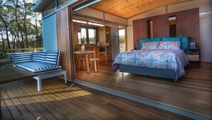 A bedroom with a bed, a desk, and a seating area on a deck. - Free Spirit Pods (North Bruny)