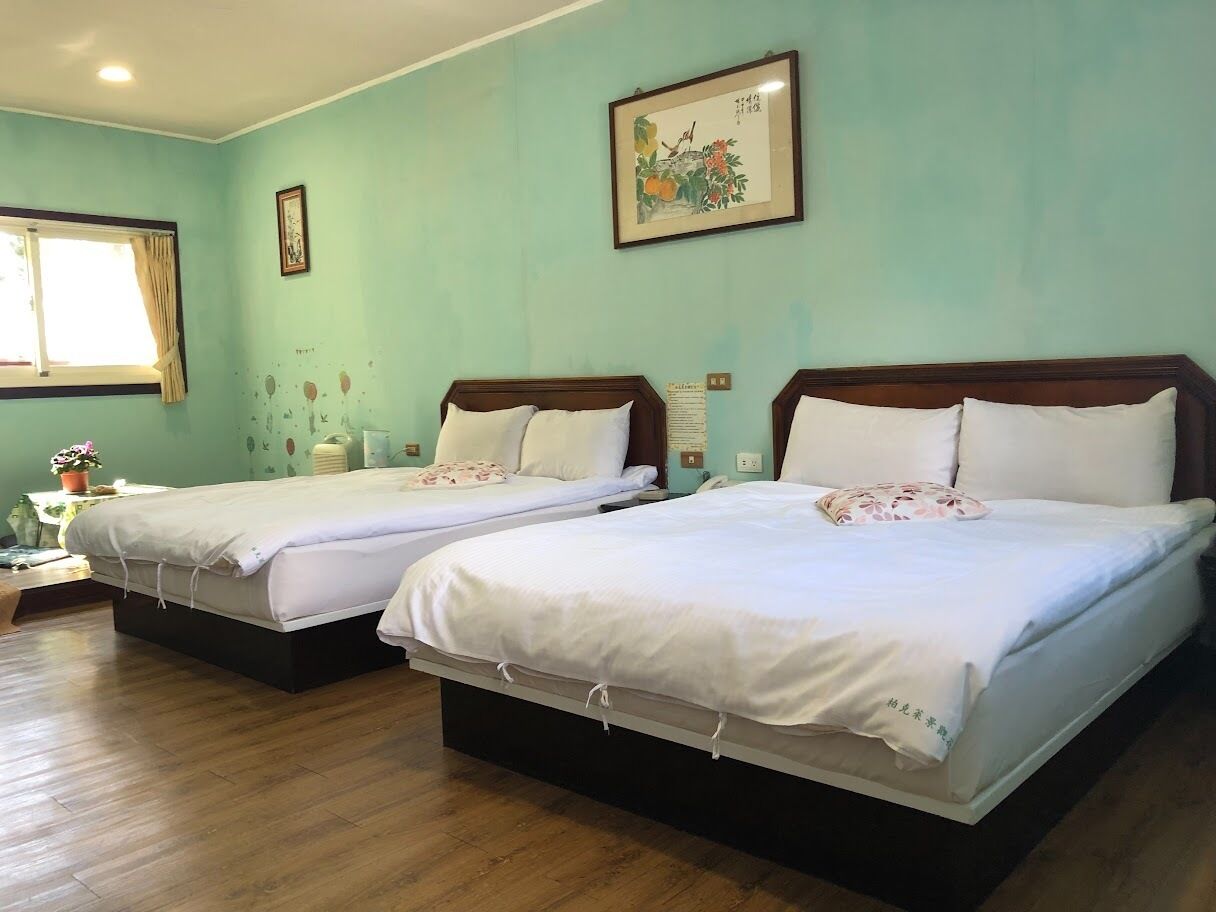 Habitación de hotel con dos camas, piso de madera, una ventana con cortinas y un cuadro colgado en la pared.
