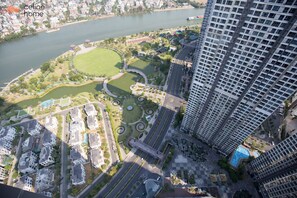 An aerial view of a modern urban area with high-rise buildings, a river, and a park with pathways and a circular water feature. - Celine Home - Vinhomes Central Park (Ho Chi Minh City)