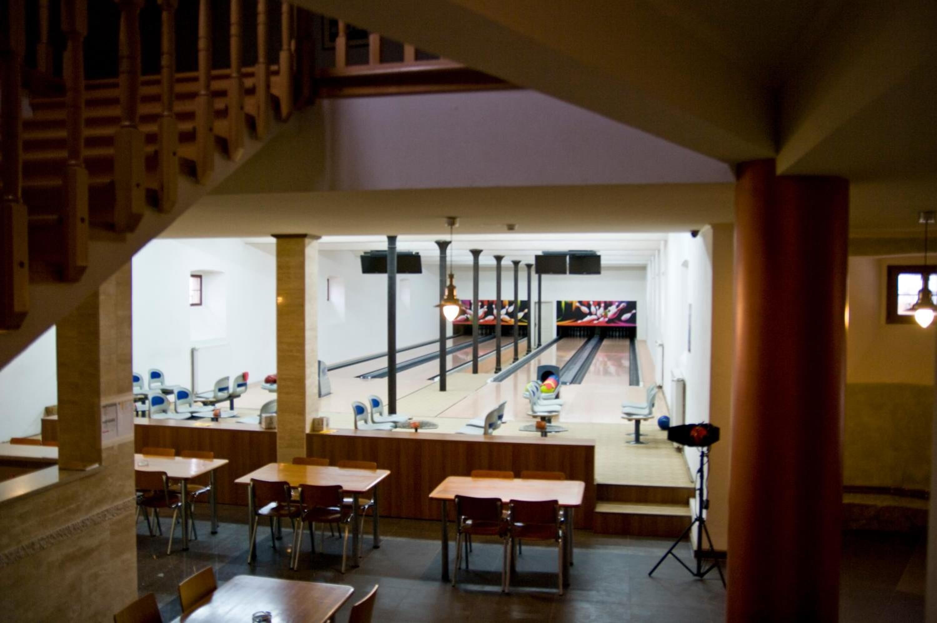 A bowling alley with multiple lanes, wooden tables, and chairs arranged in the foreground.