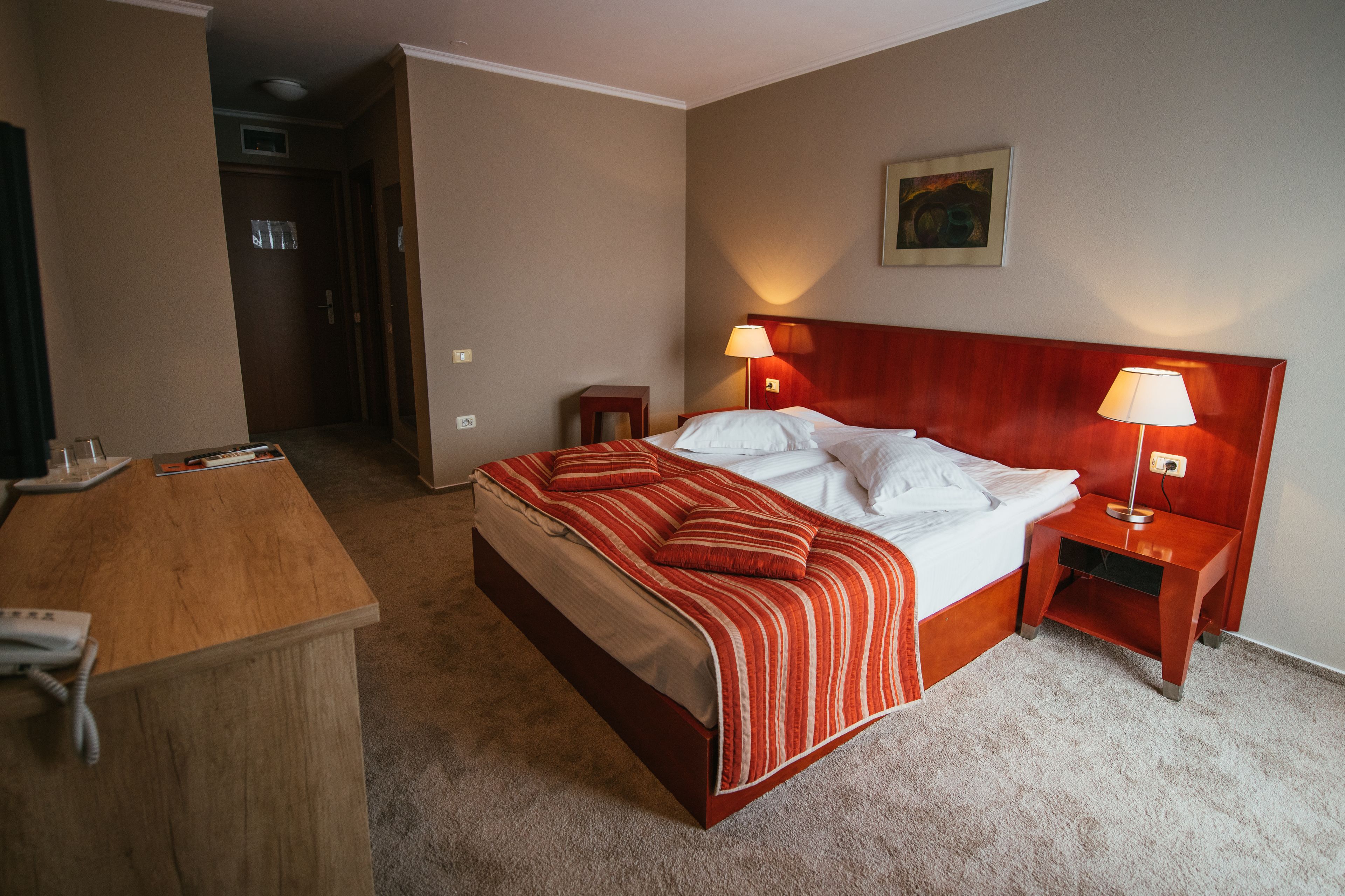 Una habitación de hotel con cama, mesitas de noche, un escritorio y teléfono.