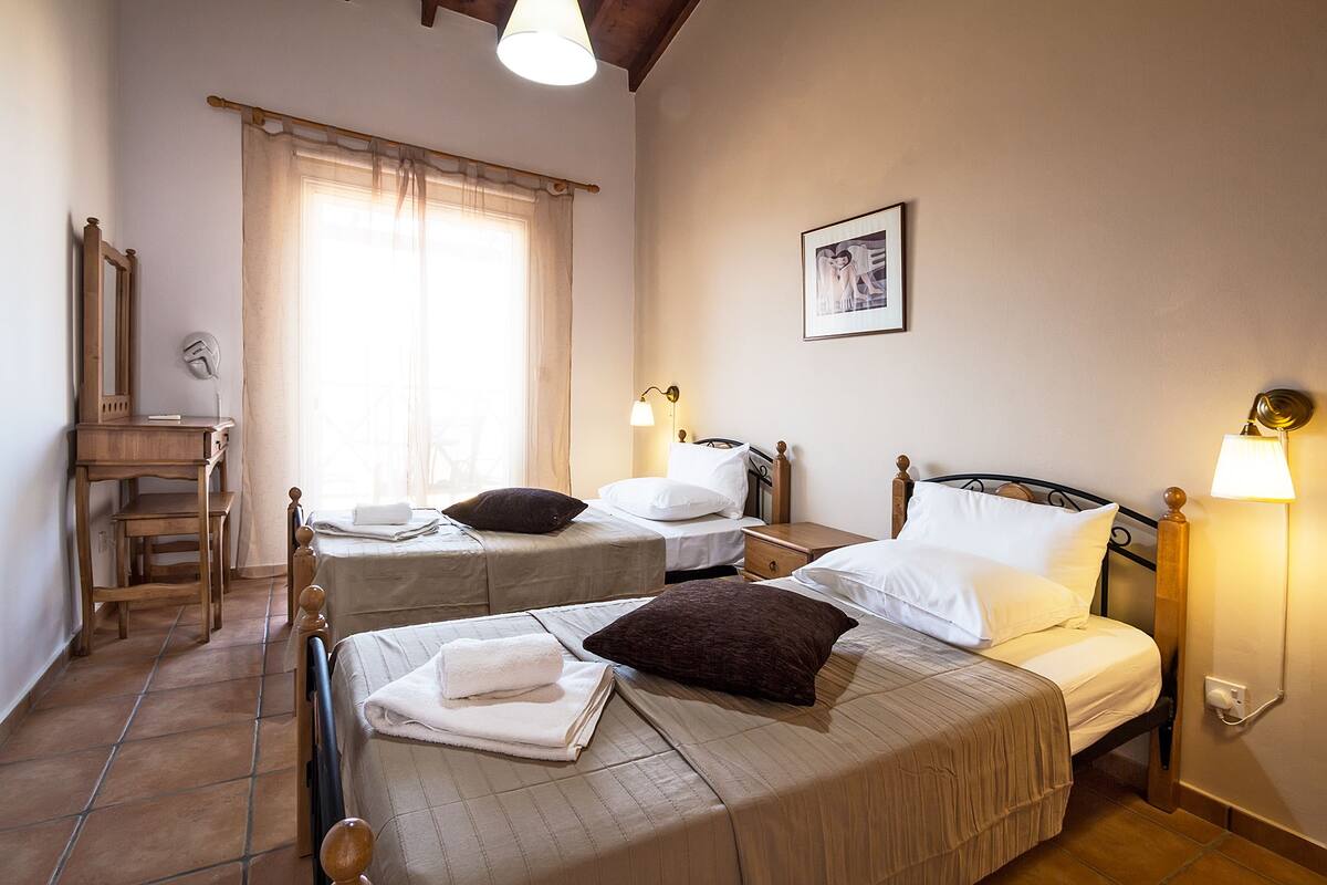 Une chambre d’hôtel avec deux lits, un bureau en bois, une chaise, une fenêtre avec des rideaux et un tableau encadré au mur.
