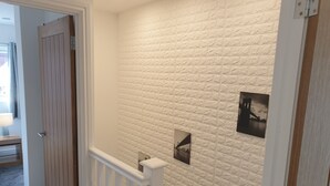 Een gang met een muur met textuur, een houten deur en een witte balustrade.