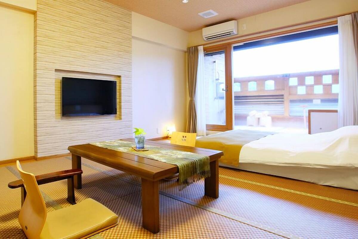 A hotel room with a bed, a desk with a chair, a TV, and a window with curtains.