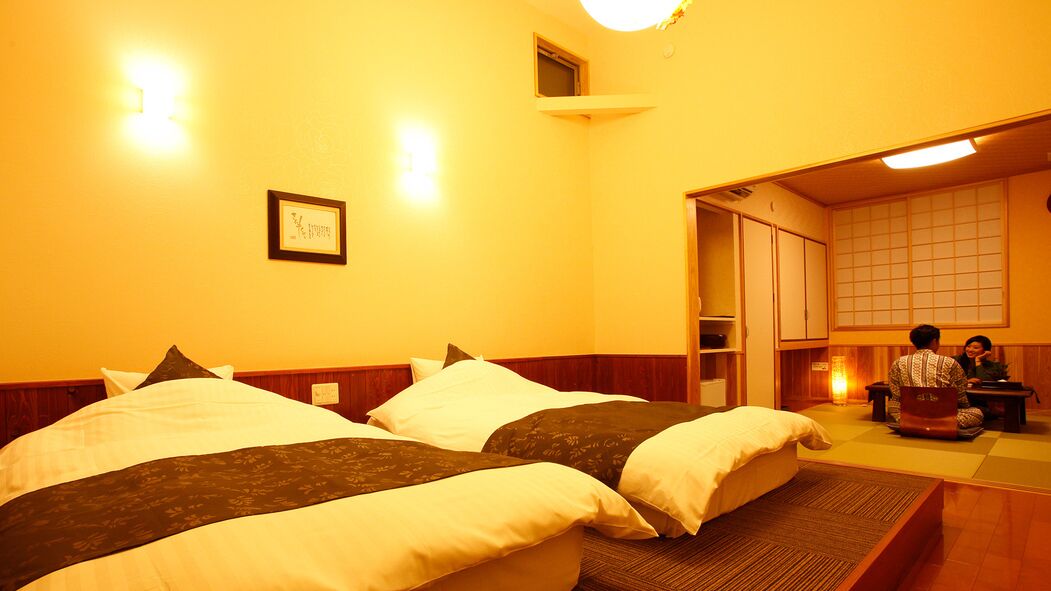 Ein Hotelzimmer mit zwei Betten, einer kleinen Sitzecke und einer traditionellen japanischen Einrichtung.