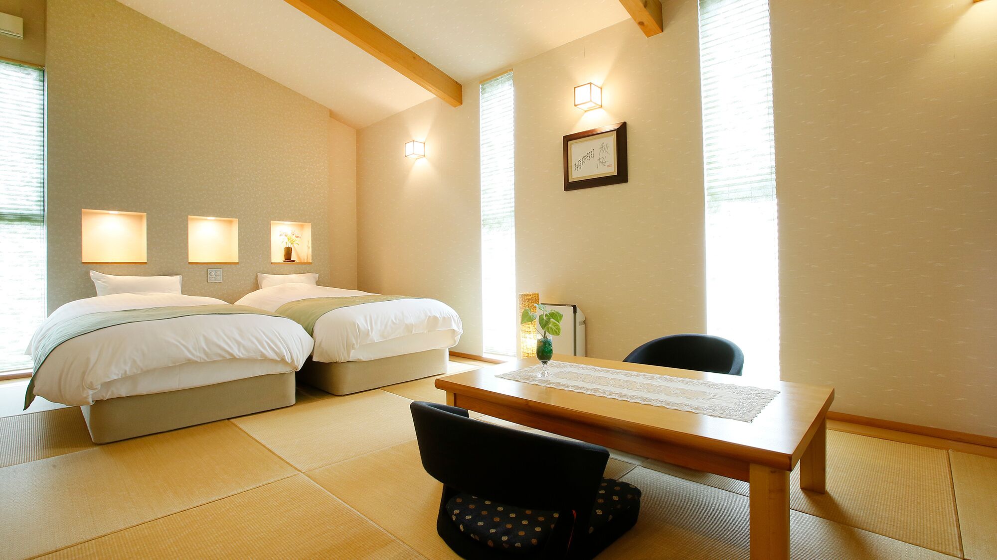 Ein Hotelzimmer mit zwei Betten, einem Holztisch, einem Stuhl und einem Schreibtisch mit einer Lampe.