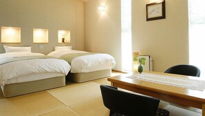 A hotel room with two beds, a desk, and a chair. There are wall-mounted lights and a framed picture on the wall. - Yuyuan (Kirishima)