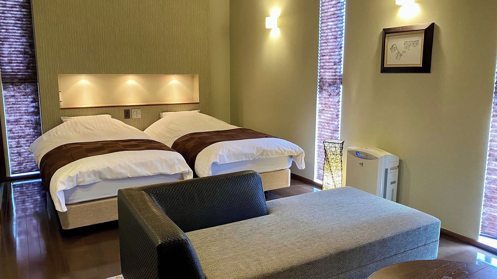 Ein Hotelzimmer mit einem Bett, zwei Nachttischen, einem Sessel, einem Schreibtisch und einer Wandlampe.