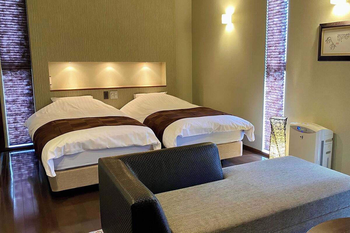 A hotel room with a bed, two bedside tables, a chair, a desk, and a wall-mounted lamp.