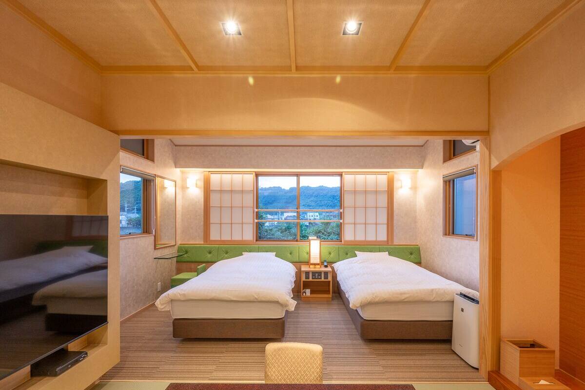 A room with two beds, a window with a view, and a small table with a lamp.
